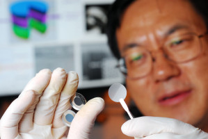 Forscher Zhong Lin Wang mit den Komponenten der auf Druck selbst ladenden Batterie: In der Pinzette piezoelektrische Film, die Pumpe für die Lithium-Ionen, zwischen den Fingern die Kapselhälften mit Anode und Kathode.