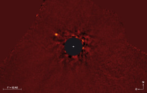 Falschfarbenbild des Sternensystems Kappa Andromedae. Das Licht des Sterns im Zentrum wurde entfernt, da er das gesamte Bild überstrahlt hätte. Der Planet zeichnet sich deutlich als heller Punkt links oben vor dem Hintergrundrauschen ab.