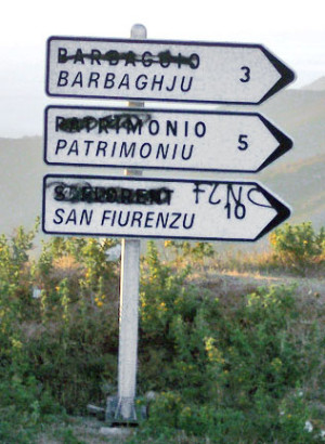 Ein Straßenschild auf Korsika: Korsisch ist ein Dialekt der Italoromania. Die nördlichen Dialekte sind mit dem toskanischen Italienisch, die südlichen mit  nordsardischen Dialekten verwandt