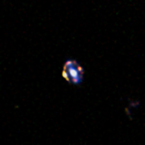 Dieses Bild zeigt die am weitesten entfernte bekannte Gravitationslinse. Die den Effekt bewirkende Galaxie befindet sich in der Mitte. Um sie herum sind mehrere deutlich verstärkte Bilder der dahinter liegenden Galaxie zu sehen.
