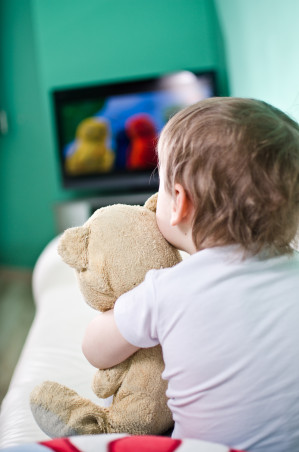 Hemmt die Entwicklung sozialer Kompetenzen: Ein Kind mit seinem Teddybär im Arm schaut Fernsehen.