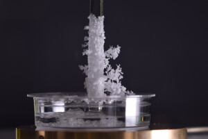 Filigran strukturierte Salzkrusten kristallisieren an einem Glasstab aus.