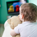Hemmt die Entwicklung sozialer Kompetenzen: Ein Kind mit seinem Teddybär im Arm schaut Fernsehen.