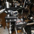 Blick auf die Hochgeschwindigkeits-Kamera mit einer mittig angeordneten Glasscheibe, von der ein Laser eine dünne Oberflächenschicht verdampft.